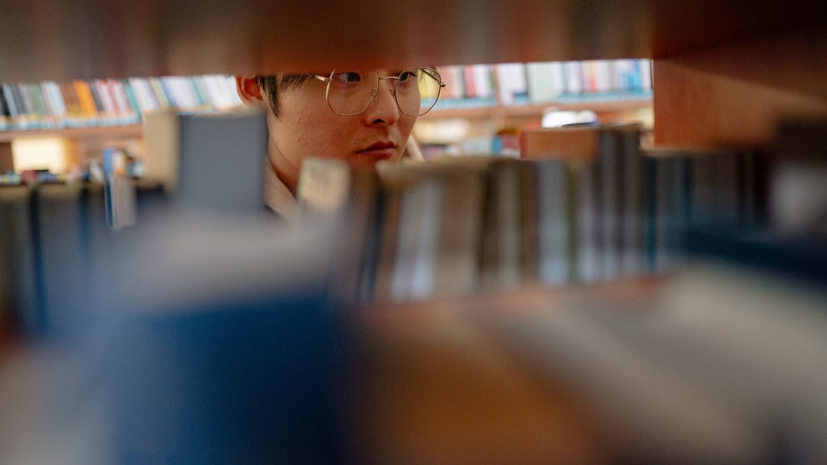 Jeune homme à lunettes lisant entre les rayonnages d'une bibliothèque